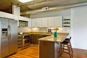 A modern kitchen with stainless steel appliances, a central island, and bar stools. - Chic Downtown LA Condo with Parking, Pool & Gym (Los Angeles)
