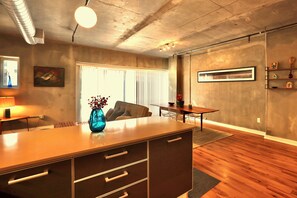 A modern kitchen with a central island, a dining area with a table and chairs, and a large window with blinds. - Chic Downtown LA Condo with Parking, Pool & Gym (Los Angeles)