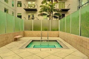 A rectangular indoor swimming pool with a single diving board, surrounded by a tiled floor and walls with a green-tinted glass partition. - Chic Downtown LA Condo with Parking, Pool & Gym (Los Angeles)