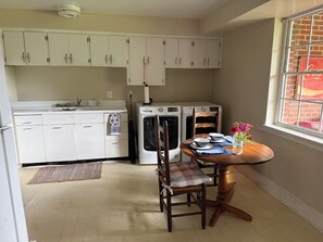 A compact kitchen with white cabinets, a washing machine, a dining table with chairs, and a window with a brick wall view. - Private apartment in quiet Athens neighborhood. Walk to UGA sports and campus. (Athens)
