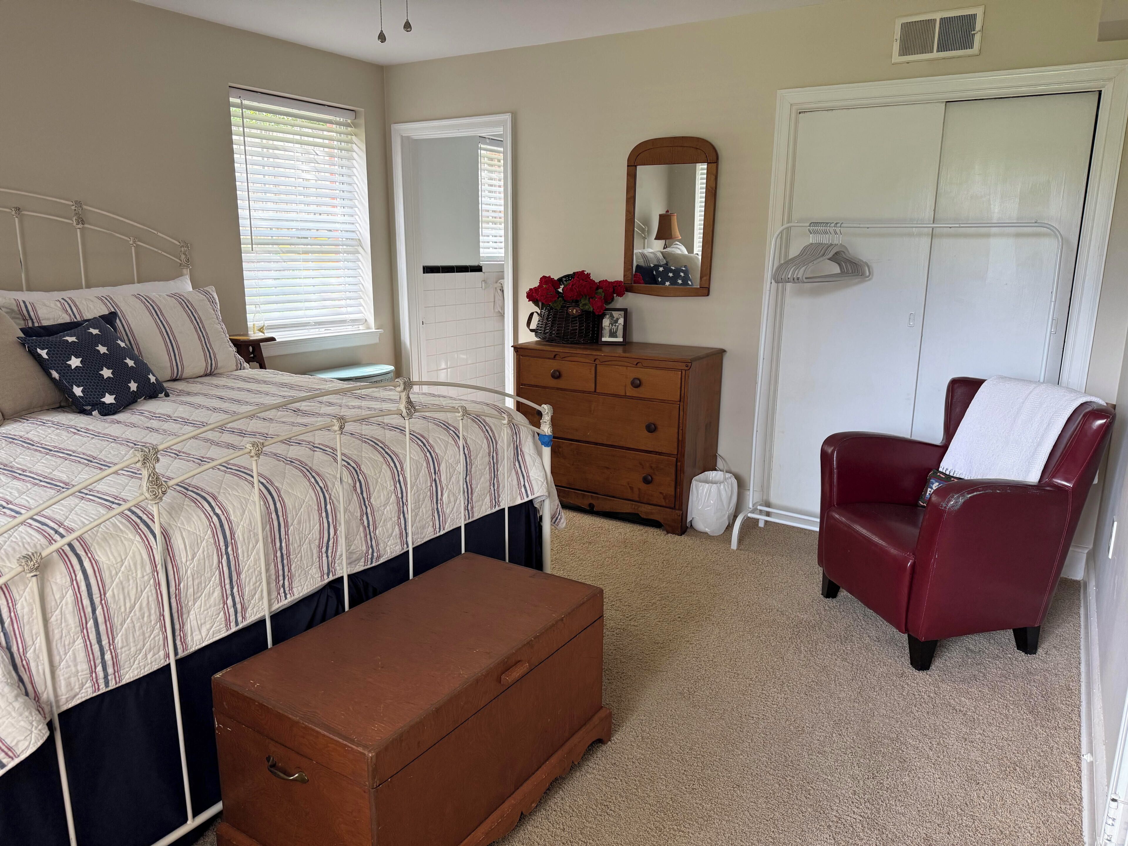 A bedroom with a bed, dresser, chair, and a closet.