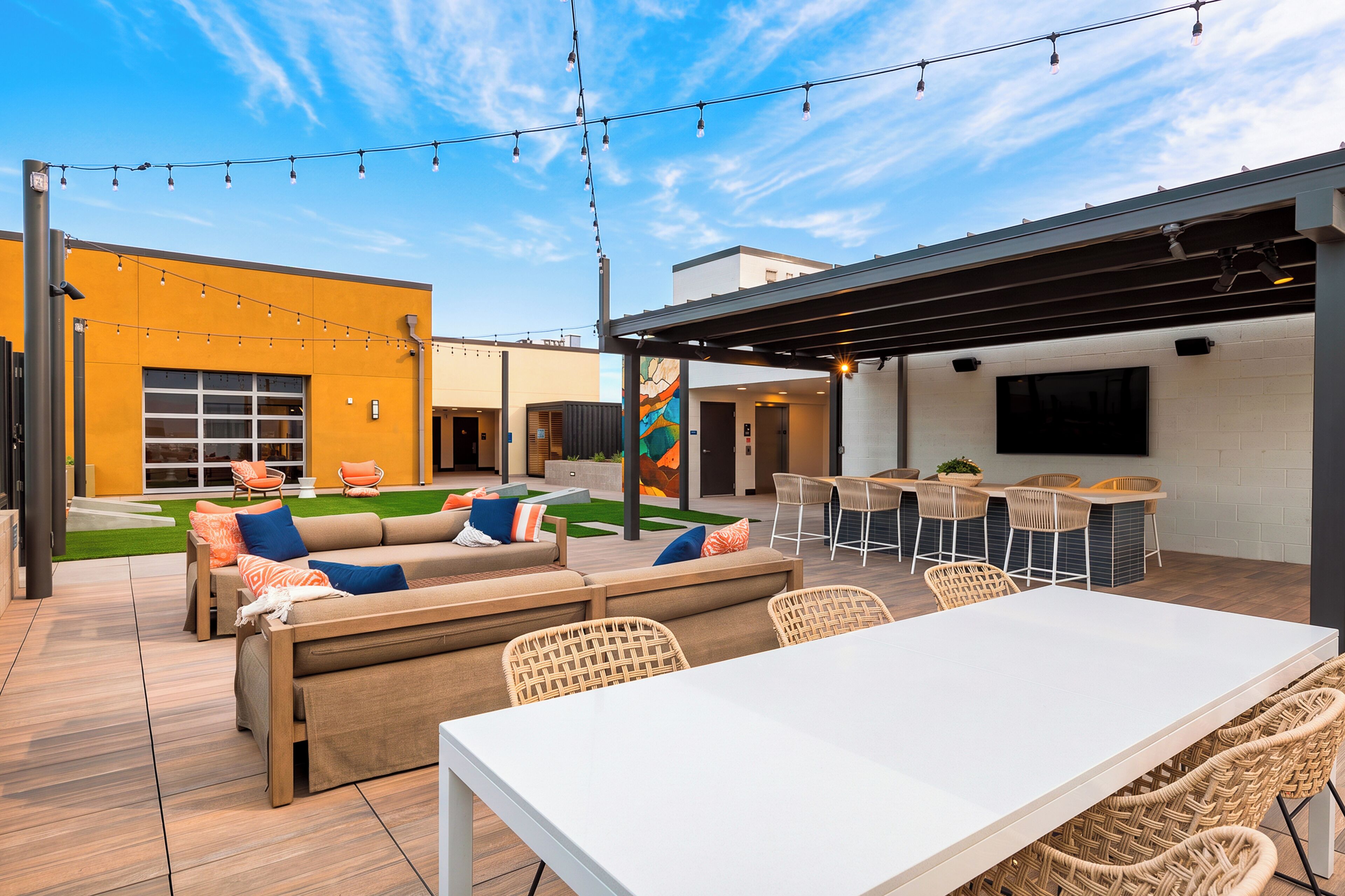 An outdoor patio area with a sofa set, dining table, and chairs, a bar area, and a building with a yellow facade.