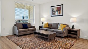 A modern living room with a sofa set, a coffee table, two side tables with lamps, a ceiling fan, and a large window with blinds.