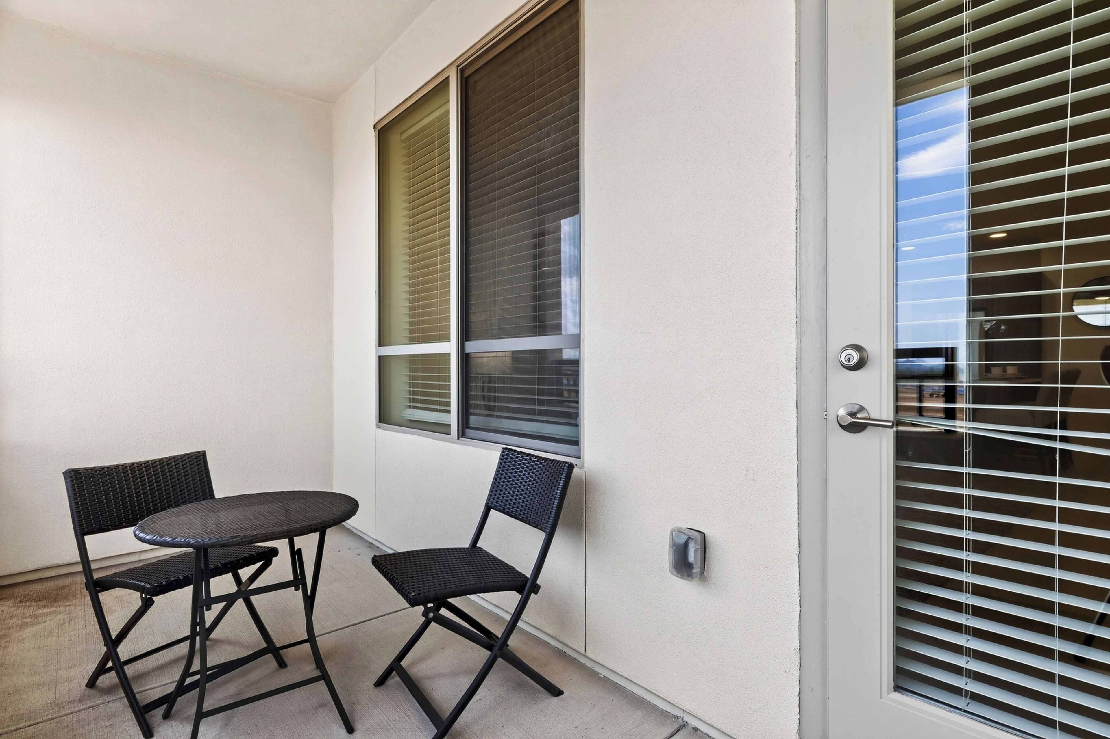Ein Balkon mit zwei Stühlen und einem Tisch, eine Tür mit Fenster sowie eine Wand mit strukturierter Oberfläche.