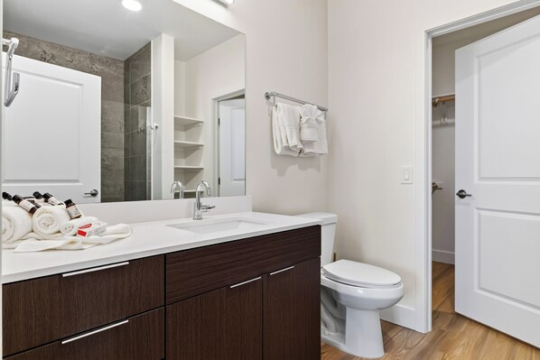 Un baño moderno con un lavabo blanco, armarios de madera oscura, un inodoro blanco y un espejo grande.