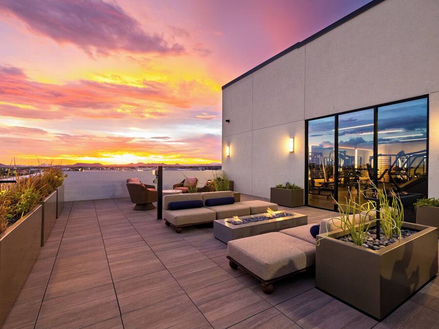 A rooftop terrace with seating, a fire feature, and a view of the sunset over the city.