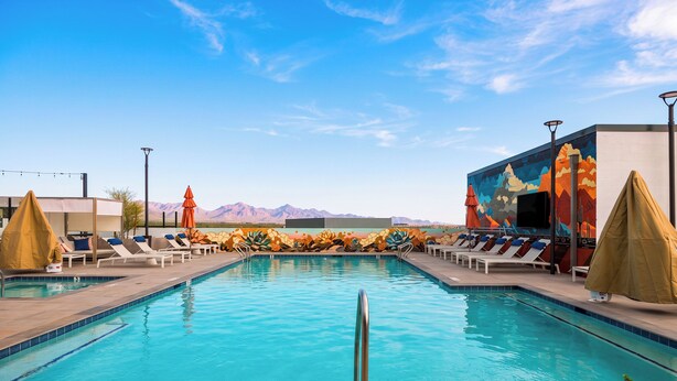 A swimming pool with lounge chairs and umbrellas, surrounded by a building with a colorful mural.