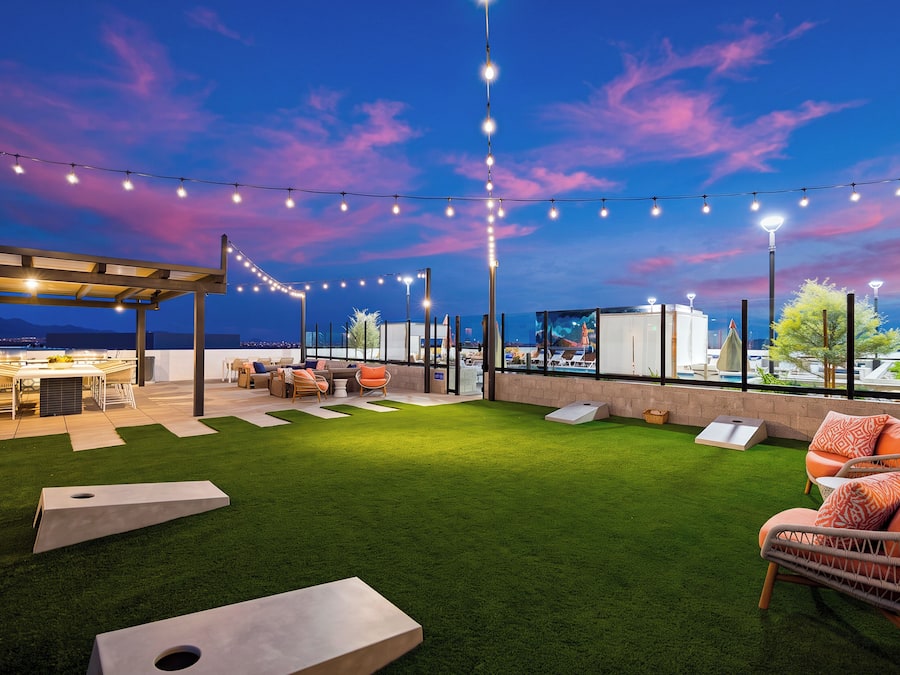 Un patio al aire libre con césped artificial, asientos e iluminación con luces colgantes bajo un cielo crepuscular.