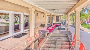 Un patio al aire libre con una mesa de vidrio, sillas anaranjadas y una zona de estar cubierta con cojines.