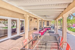 An outdoor patio with a glass table, orange chairs, and a covered seating area with cushions. - Serenity Stay in Henderson with Pool! (Henderson)
