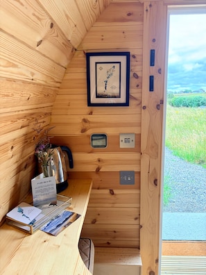 Interior de una cabaña de madera con un mapa enmarcado, un hervidor, una tarjeta y una pequeña mesa.