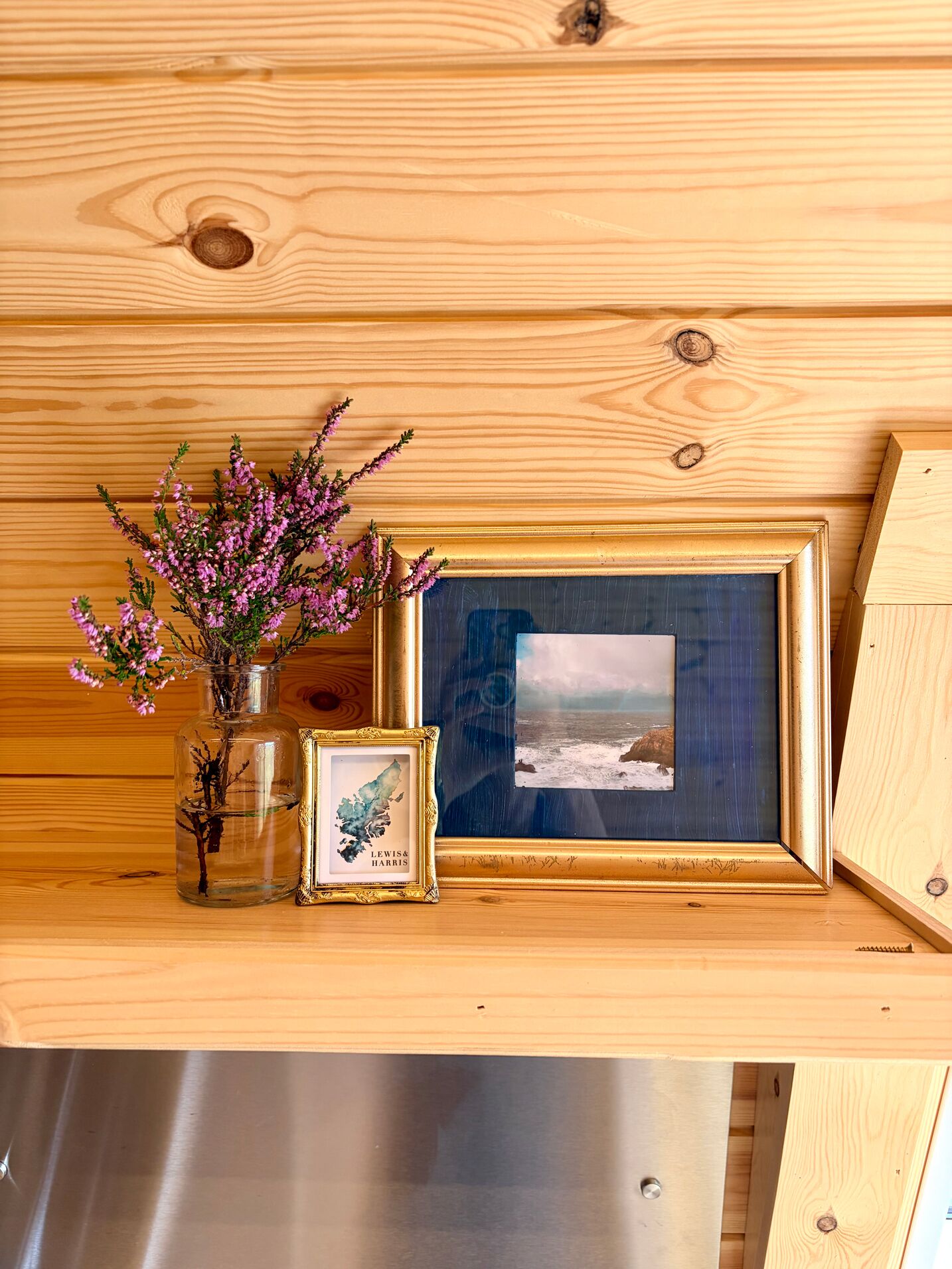 A wooden shelf with a framed picture and a glass vase with flowers.