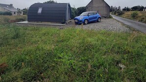 A blue car parked in front of a building with a sloped roof and a smaller shed nearby.