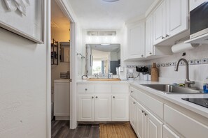 A compact kitchen with white cabinetry, a stainless steel sink, and a coffee maker. - New! Life’s a Beach! 1 BR King Suite Resort (Daytona Beach)