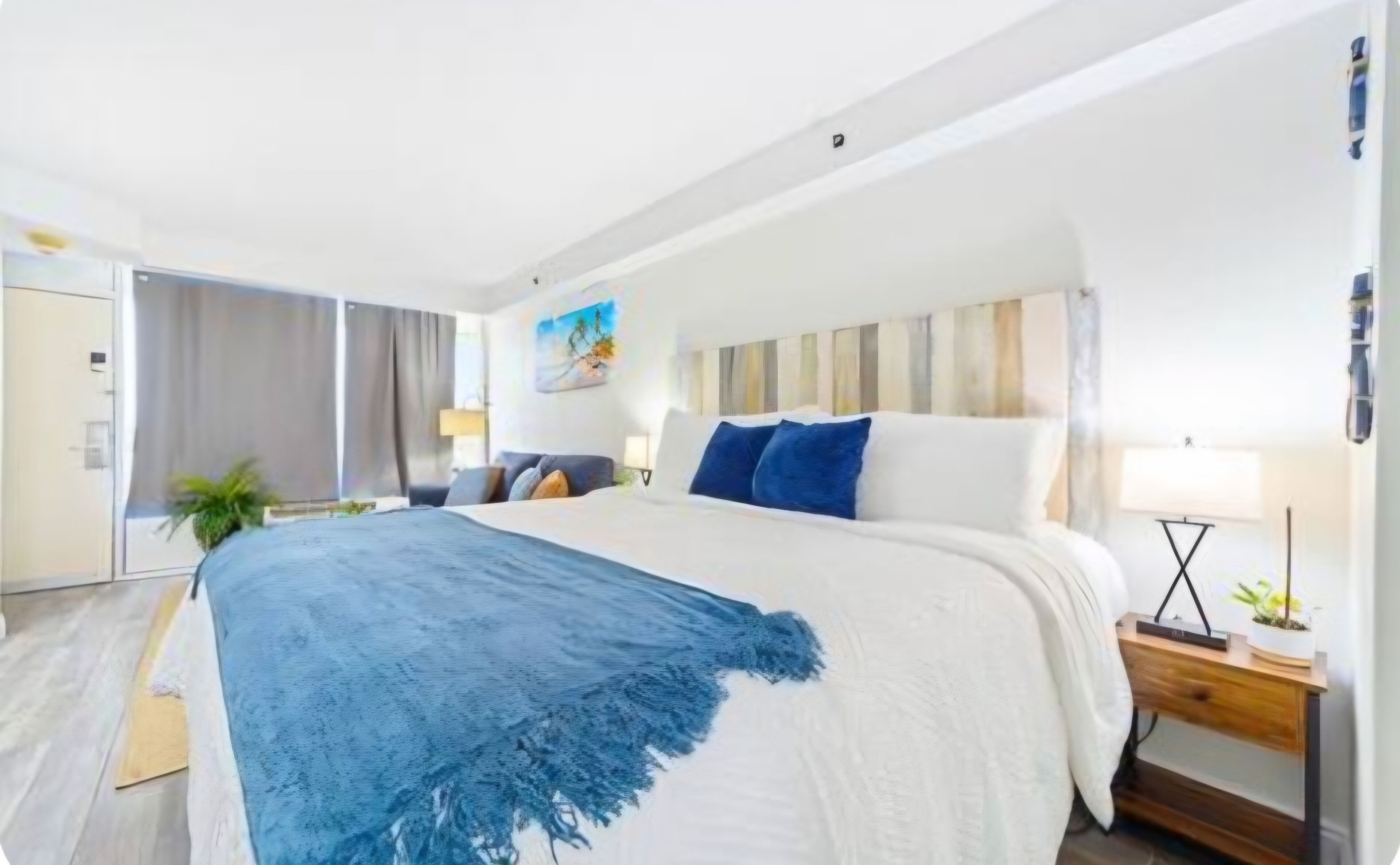 A hotel room with a large bed, a bedside table with a lamp, and a view of the outside.
