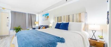 Habitación de hotel con una cama grande, una mesita de noche con lámpara y vistas al exterior.
