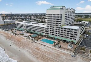A large hotel with multiple floors, a swimming pool, and a beach area. - New! Life’s a Beach! 1 BR King Suite Resort (Daytona Beach)