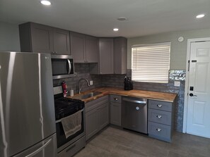 A modern kitchen with stainless steel appliances, grey cabinetry, a wooden countertop, and a window with blinds. - Serene 2-bedroom house with AC in beautiful Tucson close to Catalina adventures (Tucson)