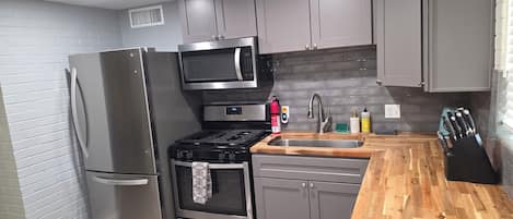 A modern kitchen with grey cabinets, stainless steel appliances, and a wooden countertop.