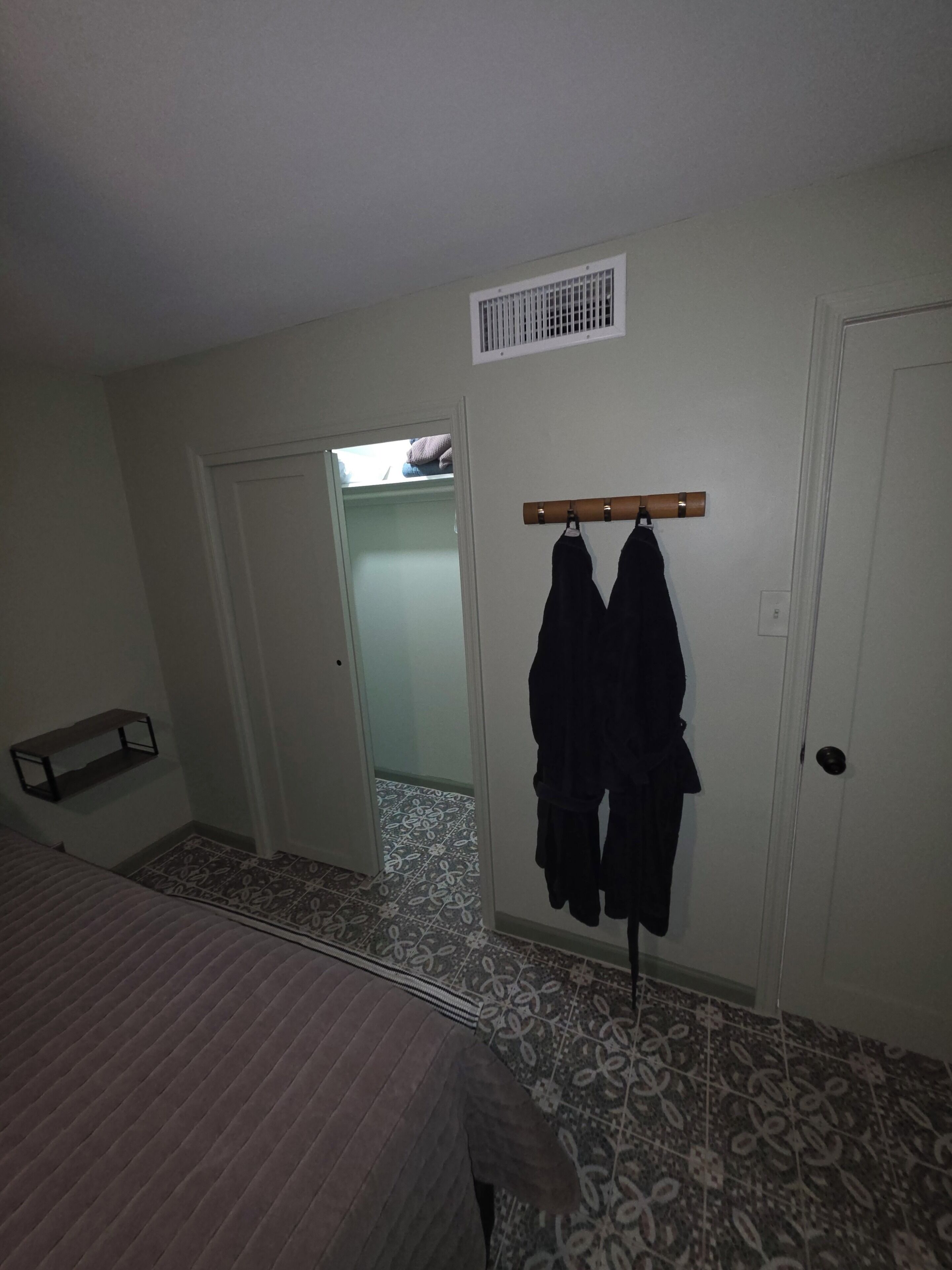 A bedroom with a bed, a wardrobe, a coat rack, and a door leading to a bathroom.