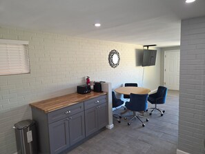 A conference room with a round table, blue chairs, a white brick wall, and a mounted television. - Serene 2-bedroom house with AC in beautiful Tucson close to Catalina adventures (Tucson)