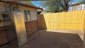 A fenced backyard with a metal utility box, a brick wall, and a wooden fence.