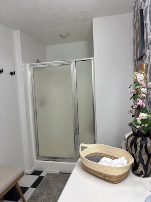 Ein Badezimmer mit Dusche, einem Waschbecken mit einer dekorativen Vase und einem Sessel.