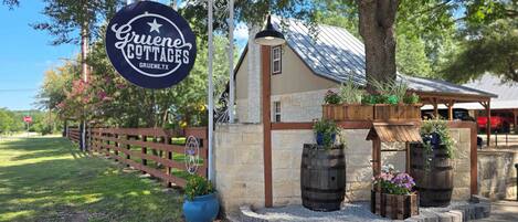 A sign for Gruene Cottages with a rustic stone building, wooden barrels, and potted plants.