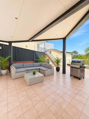 An outdoor patio with a covered seating area, a grill station, and potted plants. - Beachfront Apartment w/Ocean Views & BBQ (North Curl Curl)