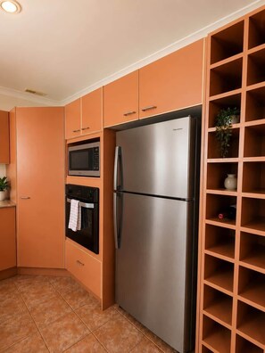A kitchen with a stainless steel refrigerator, oven, and microwave, and a wooden shelving unit with a plant. - Beachfront Apartment w/Ocean Views & BBQ (North Curl Curl)