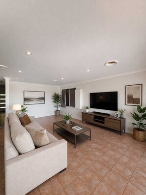 A modern living room with a sofa, coffee table, TV, and decorative plants. - Beachfront Apartment w/Ocean Views & BBQ (North Curl Curl)