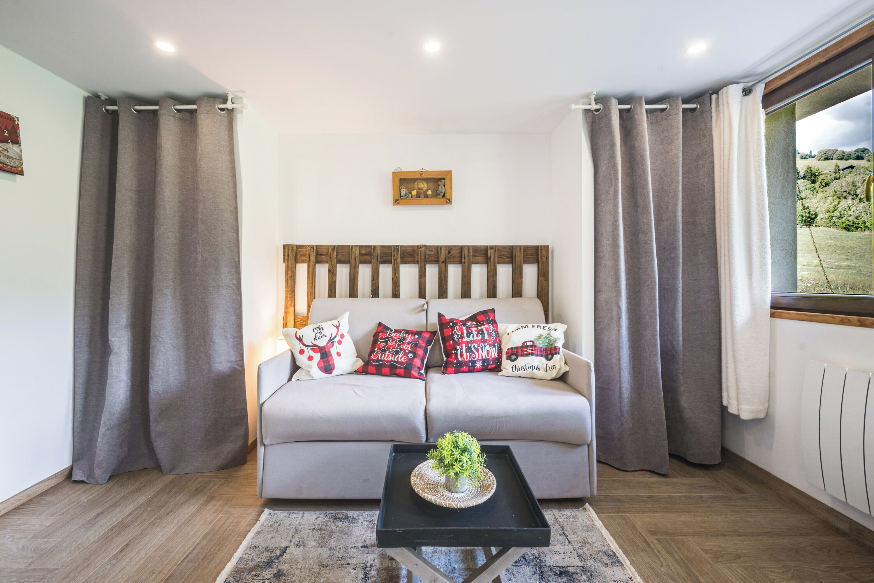 Ein modernes Wohnzimmer mit einer Couch, dekorativen Kissen, einem kleinen Tisch mit einer Pflanze und einem Fenster mit Vorhängen.