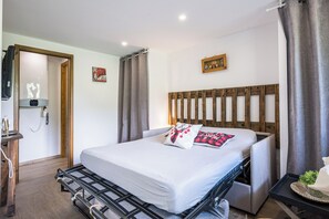 A hotel room with a bed, a headboard, a bedside table, a wall-mounted clock, and a door. - Le Flocon - Petfriendly - Proche pistes (Hauteluce)