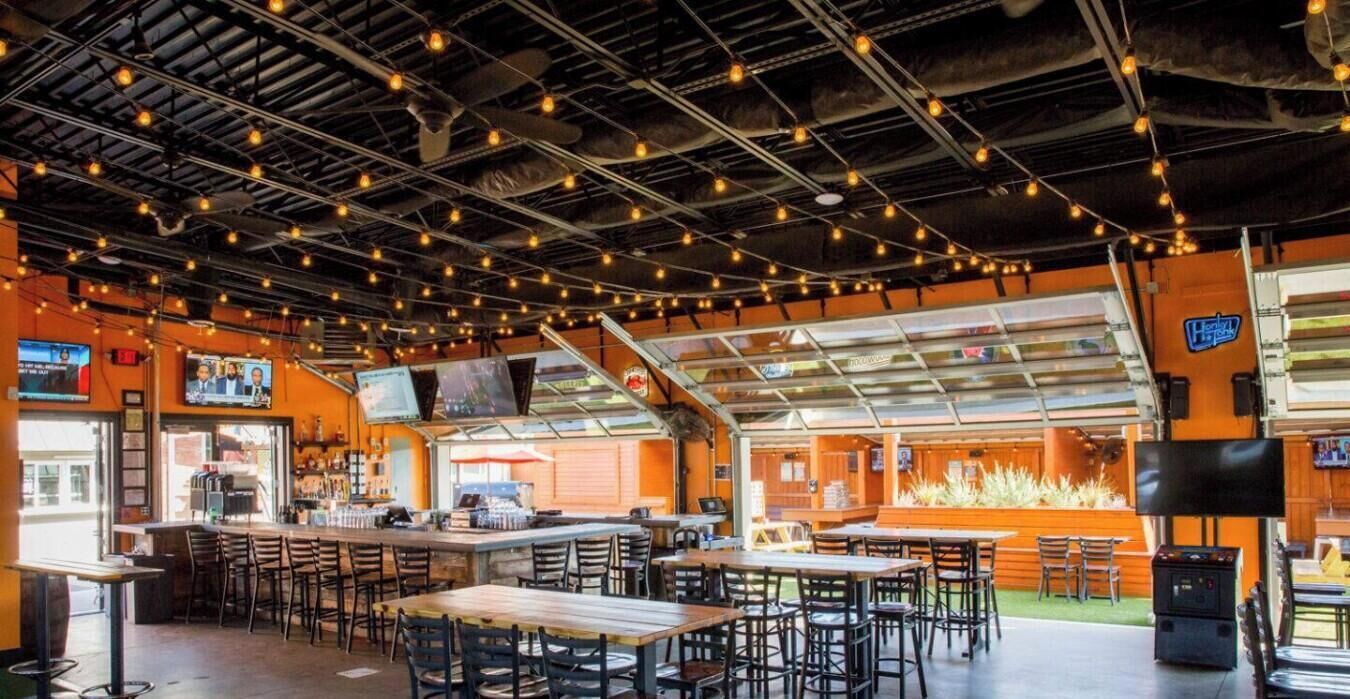 An indoor dining area with multiple tables and chairs, a bar counter, and a television screen mounted on the wall.