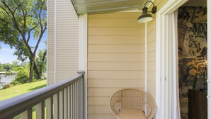 A porch with a wicker chair, a railing, and a wall with a poster. - Riverview Condo by Downtown - Pool, Free Covered Parking & Patio (Nashville)