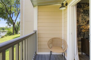 A porch with a wicker chair, a railing, and a wall with a poster.
