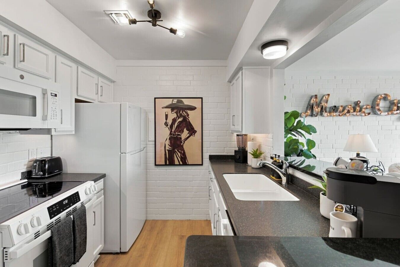 A modern kitchen with white cabinetry, a black countertop, a refrigerator, a stove, and a sink.