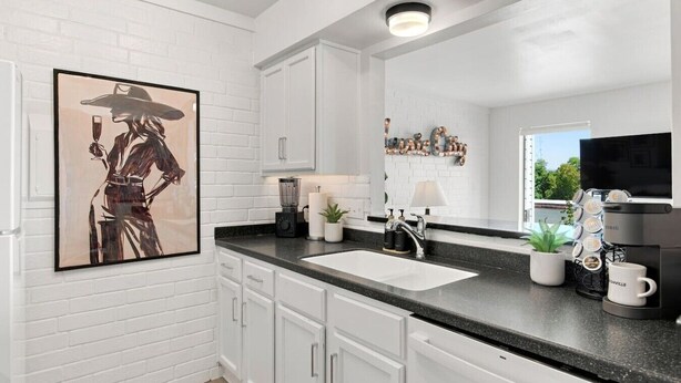 A modern kitchen with white cabinetry, a black countertop, a coffee machine, and a framed artwork on the wall. - Riverview Condo by Downtown - Pool, Free Covered Parking & Patio (Nashville)