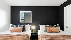 A hotel room with two beds, a nightstand, a lamp, and a window with a view of buildings. - Riverview Condo by Downtown - Pool, Free Covered Parking & Patio (Nashville)