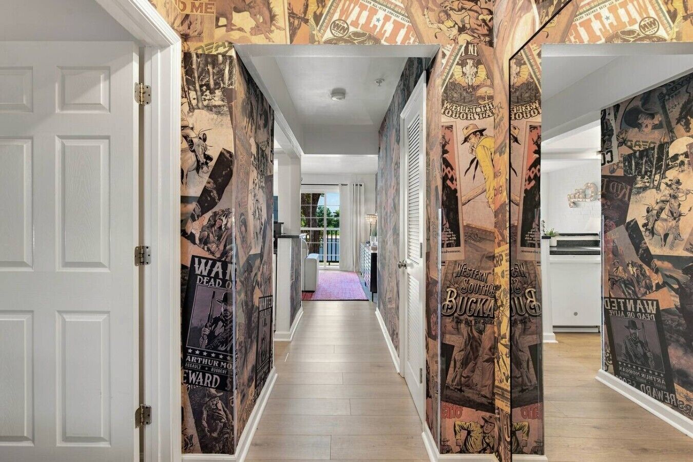 A hallway with posters on the walls, a wooden floor, and a door on the left.