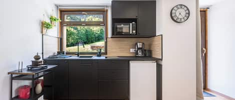 Eine kompakte Küche mit integriertem Mikrowellenherd, einer Kaffeemaschine und einem kleinen Kühlschrank.