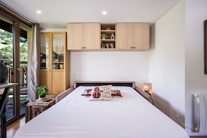 A bedroom with a bed, a nightstand, a window with curtains, and a wooden wardrobe. - Le Mont - Petfriendly - Proche pistes (Hauteluce)