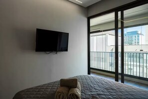 A hotel room with a bed, a flat-screen TV mounted on the wall, and a large window offering a view of the city. - Studio Tower B · view · garage · Syrian 2min (São Paulo)