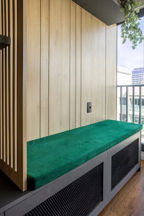 A room with a green cushioned bench, wooden panel walls, and a window overlooking a building. - Studio Tower B · view · garage · Syrian 2min (São Paulo)