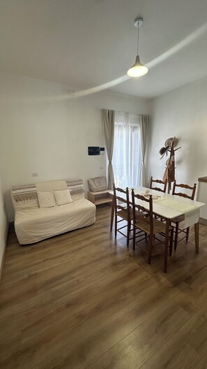 A living room with a sofa, dining table, chairs, and a ceiling light. - Domu Fanari Vacation Home in Sardinia (Assemini)