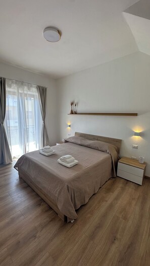 A bedroom with a bed, bedside tables, a nightstand, a window with curtains, and a ceiling light. - Domu Fanari Vacation Home in Sardinia (Assemini)