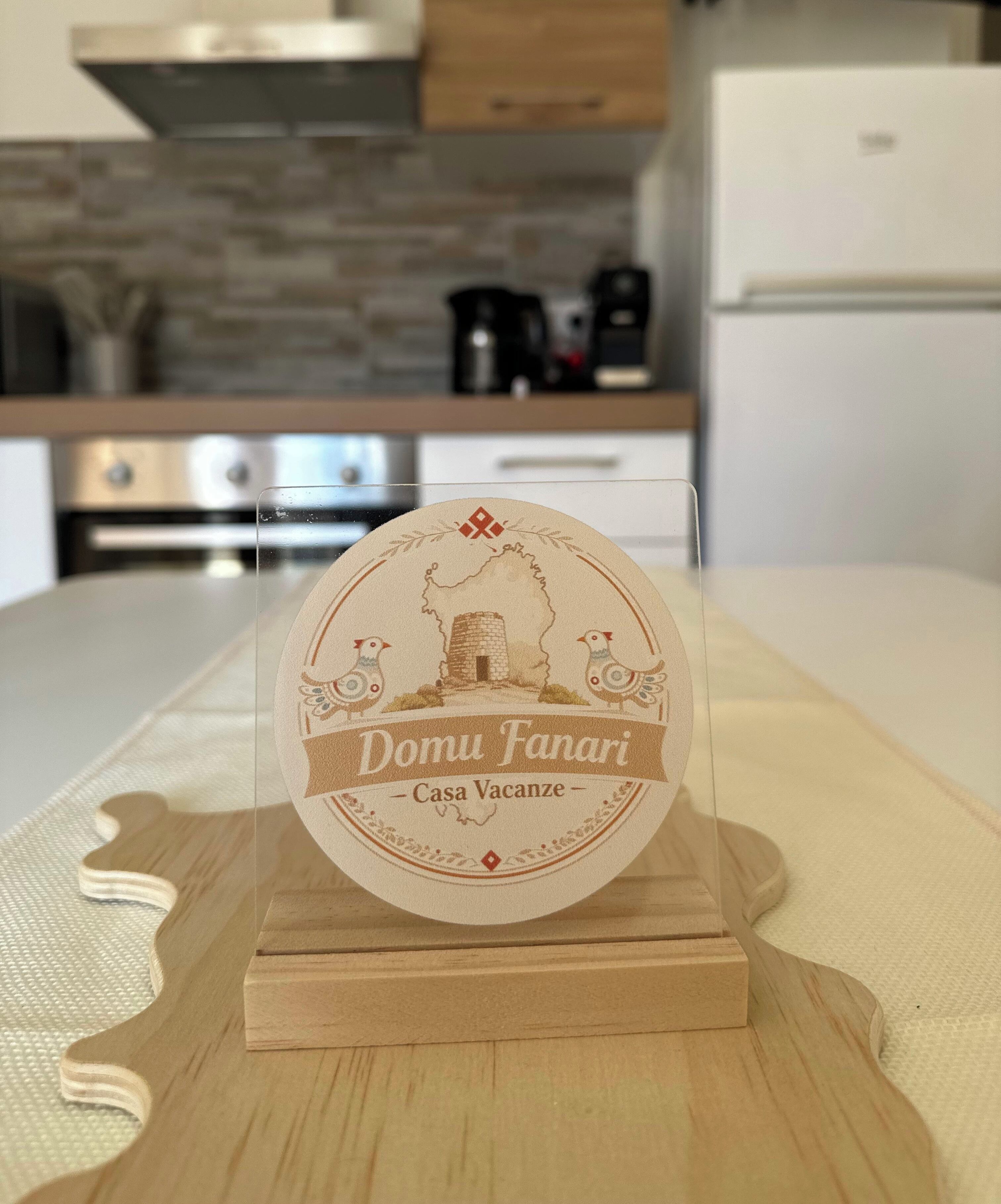 A wooden stand with a circular plaque featuring a bird and a building, labeled 'Domu Fanari - Casa Vacanze.'