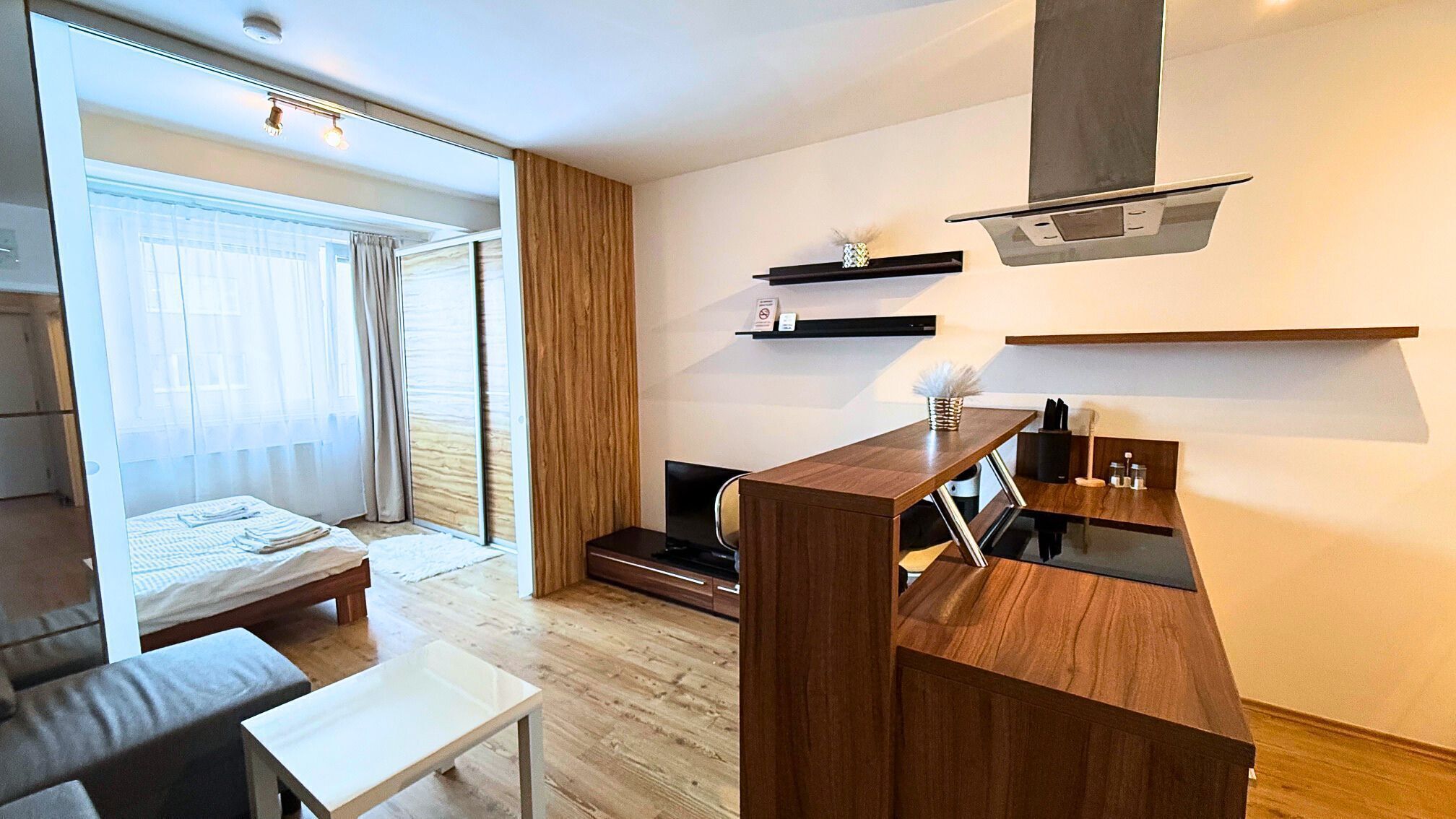 Een moderne hotelkamer met een bed, een tafeltje, een televisie en een kitchenette.