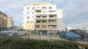 A multi-story residential building with a gated entrance, parked cars, and a hedge in the foreground. - Modern 1,5 - room apartment, Kadnárova 91 - Rača (Bratislava)