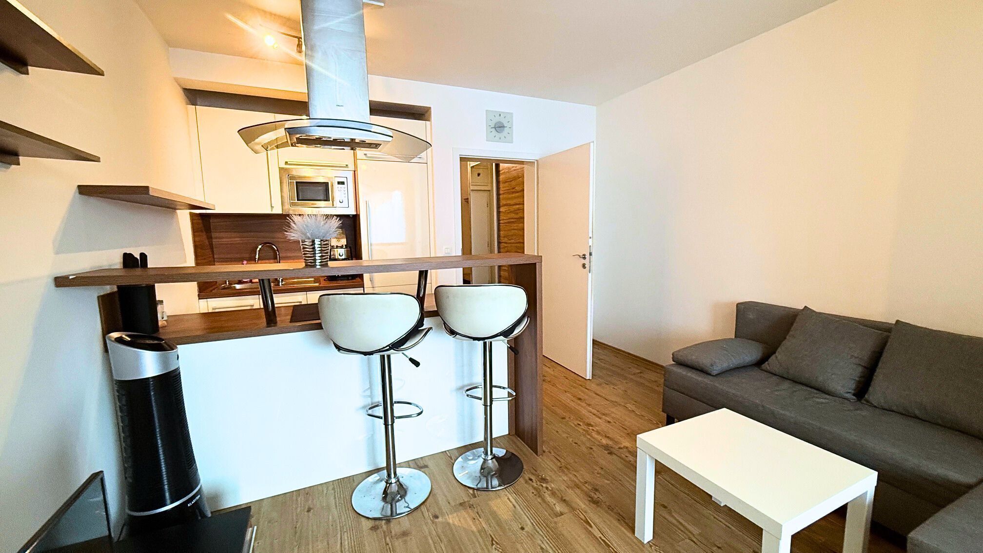A modern kitchen with a microwave, a stainless steel range hood, and a bar stool area.